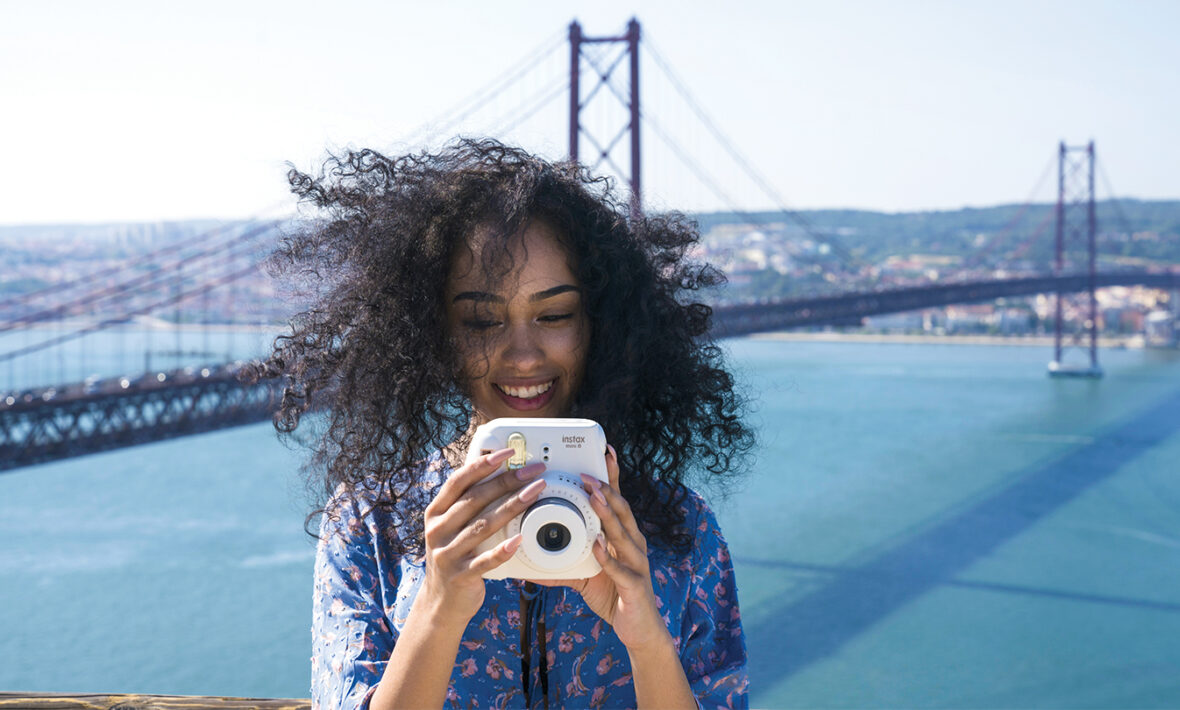 A woman is taking a picture with her camera in front of a bridge, showcasing one of the safest countries to travel solo.