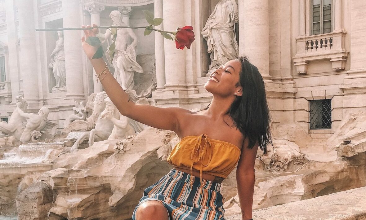 A woman holding a rose at the Trevi Fountain.