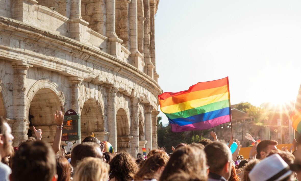 A group of people waving a rainbow flag in front of an ancient building.