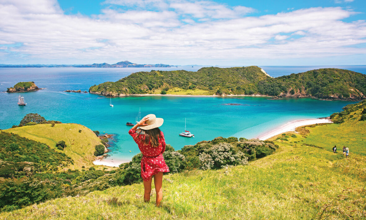 A woman is standing on a hill overlooking the ocean in one of the happiest countries.