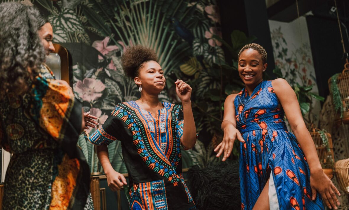 A group of African women dressed in colorful dresses dancing in a room.