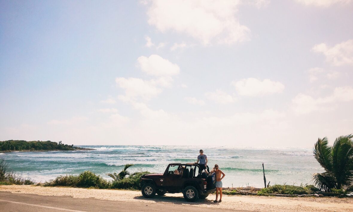 Two people enjoying one of the best road trips in the world standing on top of a jeep in front of the ocean.