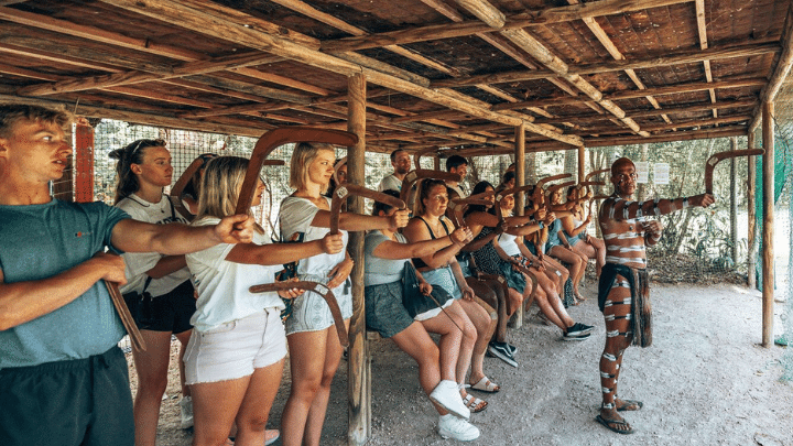 A group of First Nations people standing in front of a wooden hut.