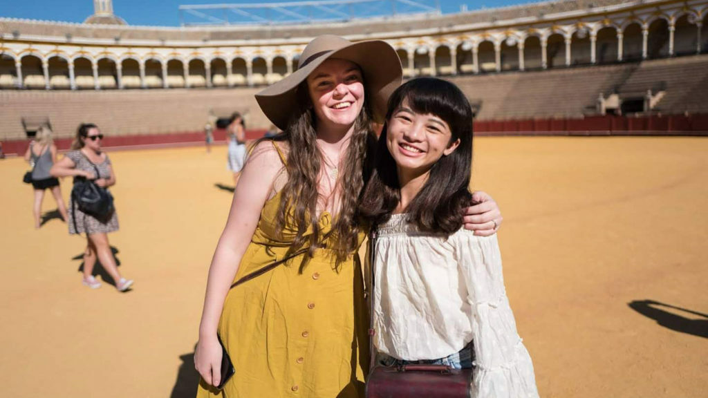 Two women solo traveling, posing in front of an arena.