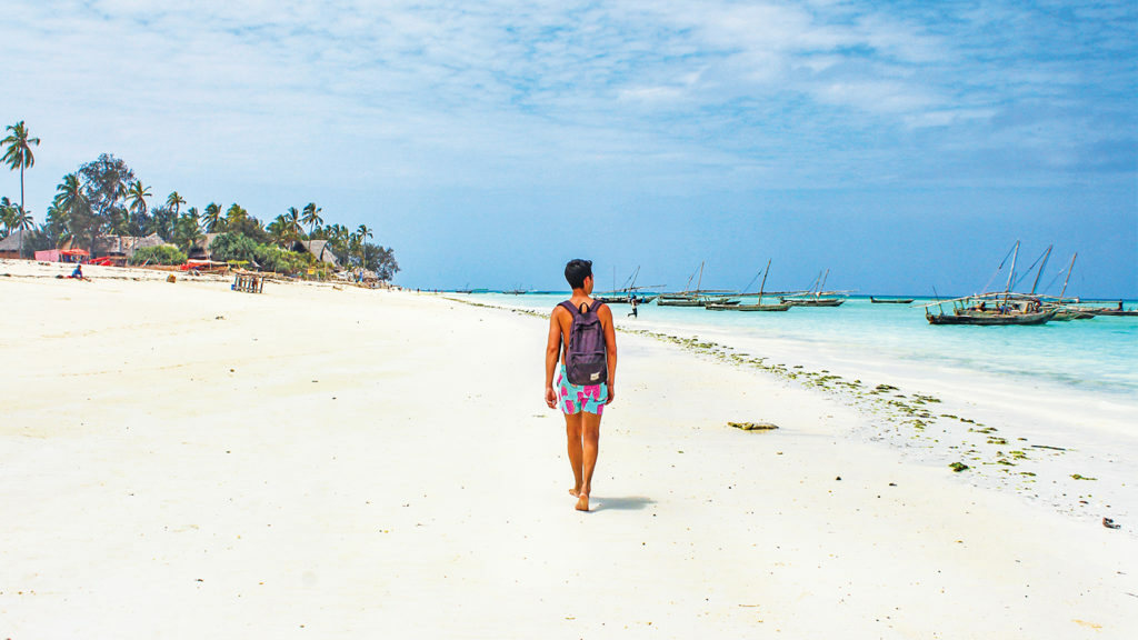 A woman walking on a white sandy beach in Tanzania.