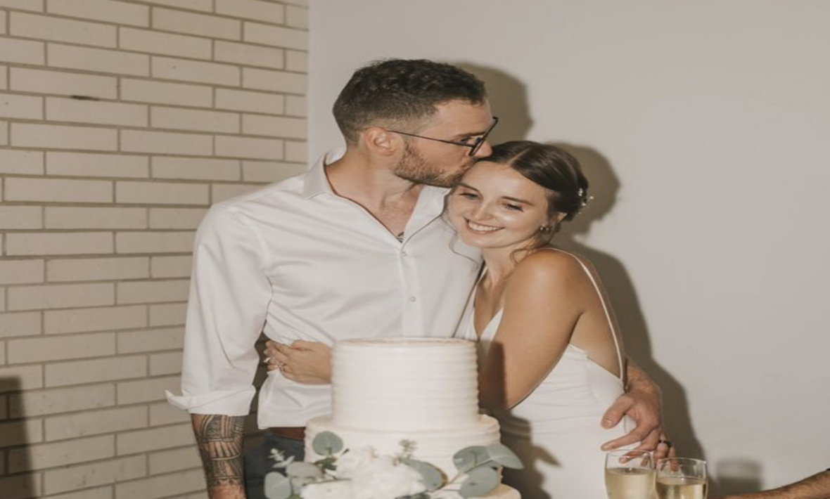 A real love story unfolds as the bride and groom share a tender kiss in front of their exquisite wedding cake.