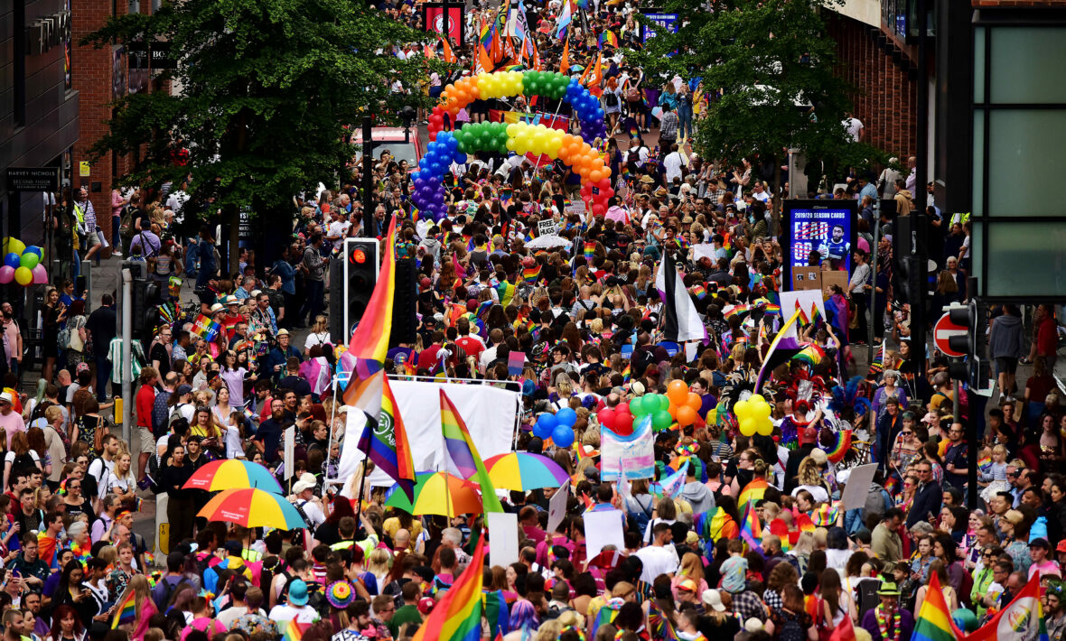 A crowd of people participating in a pride event, proudly walking down a street with rainbow flags.