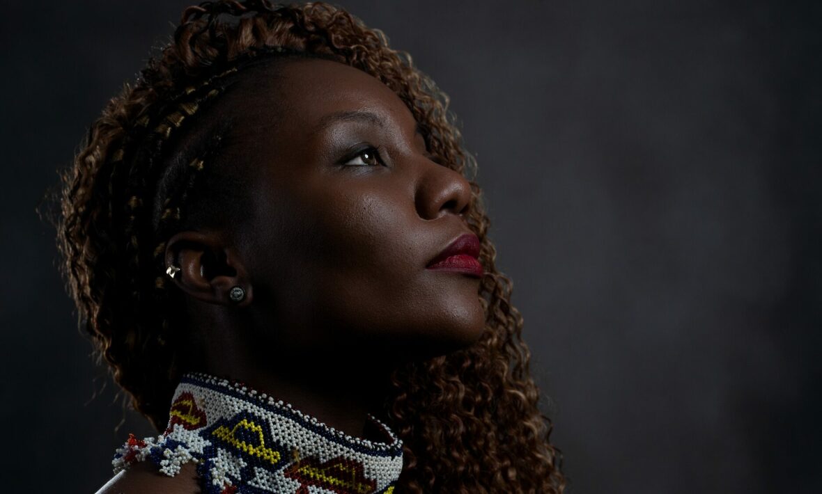 A woman with curly hair is looking up at a vibrant LGBTQIA+ travel poster against a dark background.