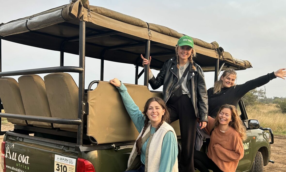 Four women on a trip to South Africa posing on the back of a safari vehicle.