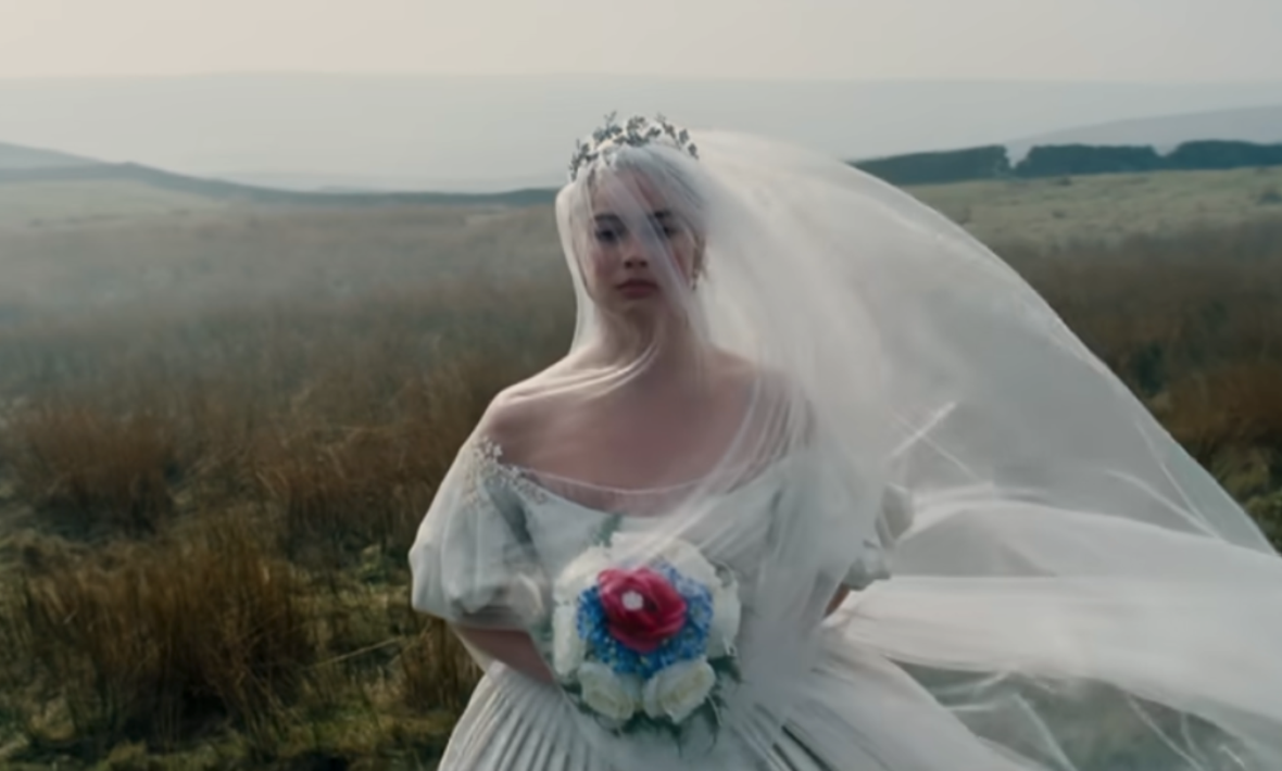 Margot Robbie in field carrying bouquet and dressed in white wedding gown in Wuthering Heights