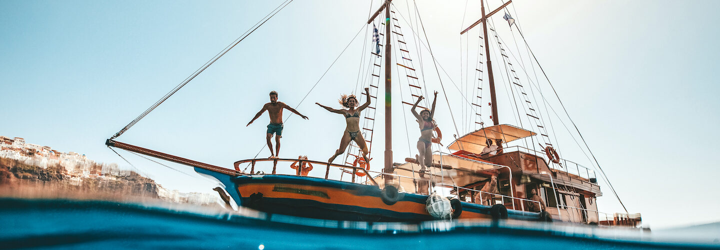 Friends jumping off boat into water having fun in Europe