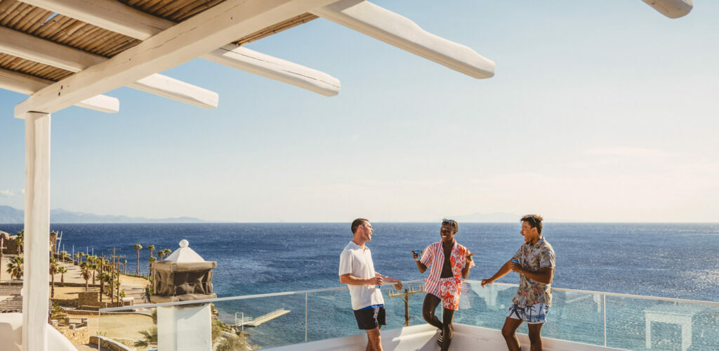 Three men standing on a balcony overlooking the ocean in Greece.