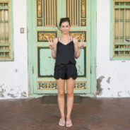 A woman in a black dress standing in front of an old building during her south east Asia travel.