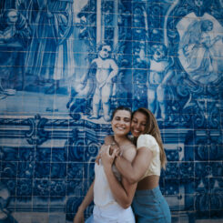 Two women hugging during their travel adventure in front of a blue tiled wall.