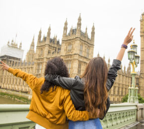 Two women waving in front of the Houses of Parliament