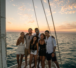 Young people standing on sailboat foredeck at sunset