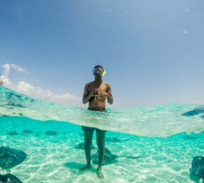 A man travels and snorkels in the water with stingrays.