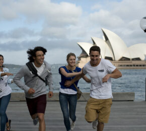 A group of people running on a pier beside the stunning Sydney Opera House, with mesmerizing views of beaches and reefs in the background.