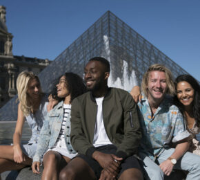 A group of Contiki age people posing in front of the Louvre pyramid.