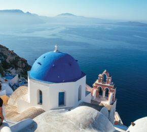 A man with a travel style is standing on a cliff overlooking the ocean.