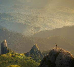 A person is standing on top of a rock, feeling inspired by the vastness of travel and adventures.