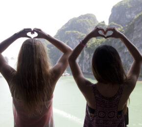 Two women using dating apps and making a heart shape with their hands.