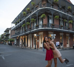 Women smiling at a crossroads with decorative American building