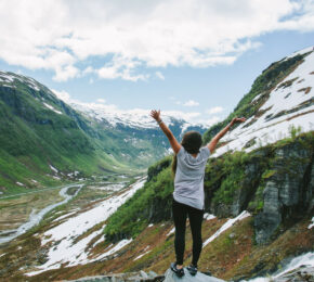 A woman standing on top of a mountain in the happiest country in the world with her arms raised.