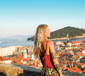 A woman quit the 9-5 and is standing on top of a wall overlooking the city of Dalmatia.