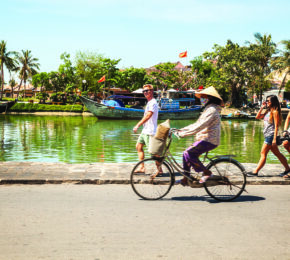 A group of people riding a bicycle near a body of water, seeking a cure for a break-up through adventure and camaraderie.