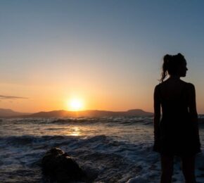 A silhouette of a woman standing on the beach at sunset.