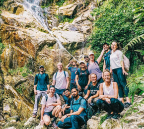 A group of people travelling and posing in front of a waterfall.