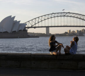 Two women sitting on a wall in front of the Sydney Opera House, job-inspired move.