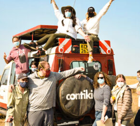 A group of people standing on top of a truck during an African safari experience in the middle of a field.