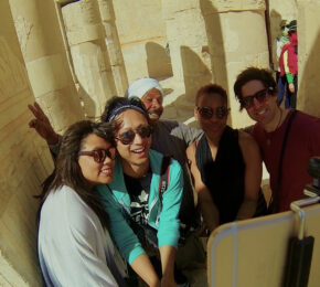 A group of people are posing for a photo in front of a ancient egyptian temple during their travels.