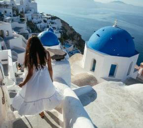 A woman in a white dress walking down the stairs in Santorini, Greece promotes brain health.