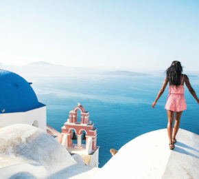 A woman is solo travelling on top of a hill overlooking the ocean.