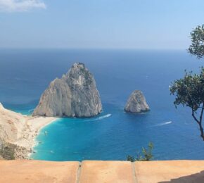 A view of a beach from a window in an old building with Greek food.