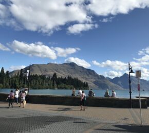 A group of people walking on a sidewalk near a lake.