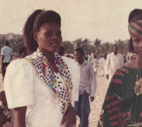 Two African women in traditional clothing standing on the beach.