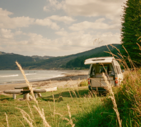 A camper van parked on a grassy hill next to the ocean.