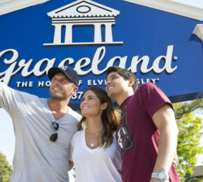 Three people taking a picture in front of the Graceland sign, representing Tennessee's music history.