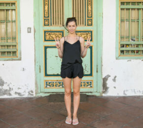 A woman in a black dress standing in front of an old building during her south east Asia travel.