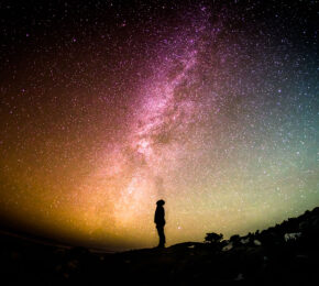 A person standing on a rock gazing up at the milky way, experiencing astrotourism.