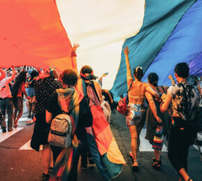 A group of LGBTQ+ individuals holding a rainbow flag in Spain.