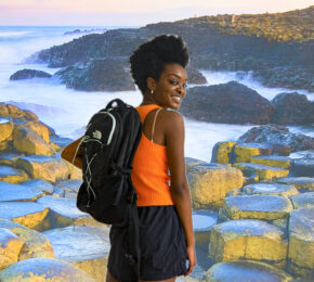 A woman with a backpack standing on a rock in front of the ocean.