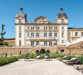 A large stone Contiki Château building is in the middle of a courtyard with lounge chairs and umbrellas.