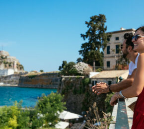 A free-spirited couple standing on a balcony overlooking the water.