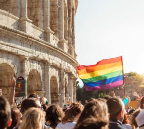 A group of people waving a rainbow flag in front of an ancient building.