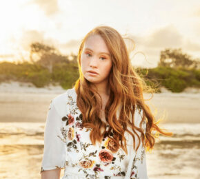 A girl in a floral dress standing on the beach at sunset, Madeline Stuart.